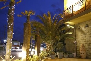 Un edificio con fachada de piedra, un balcón con barandilla de hierro forjado y plantas en macetas.