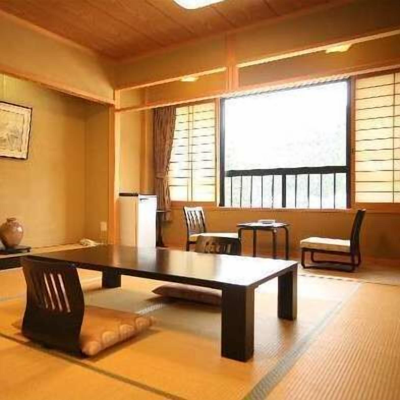 A traditional Japanese room with tatami flooring, a low table, chairs, and a window with shoji screens.