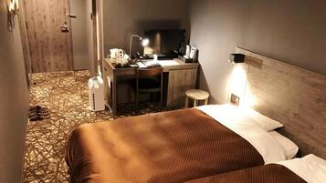 A hotel room with a bed, a desk with a computer, a chair, and a small stool.