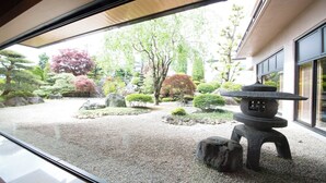 A traditional Japanese garden with a stone lantern, rocks, and various trees.