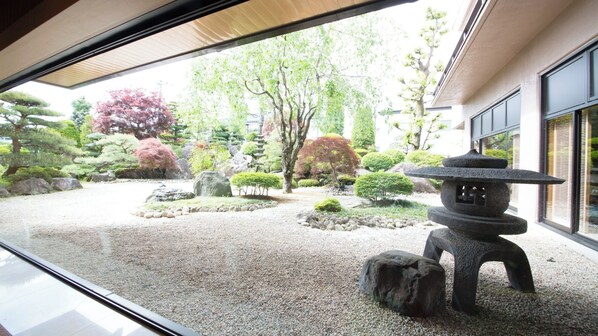 Un jardin japonais traditionnel agrémenté d’une lanterne en pierre, de rochers et de divers arbres.