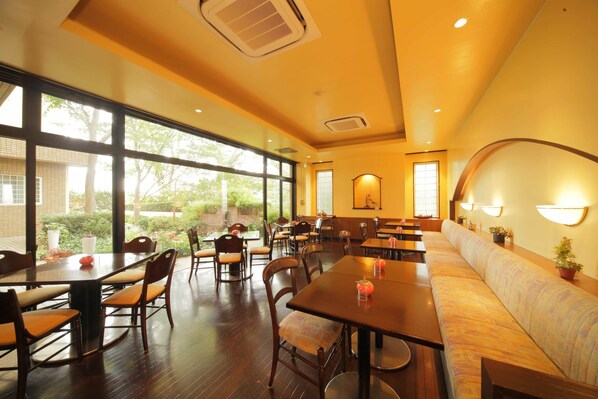 A restaurant with wooden tables and chairs, a long bench, and large windows offering a view of the outdoors. - Petit Hotel Clanvert (Hagi)