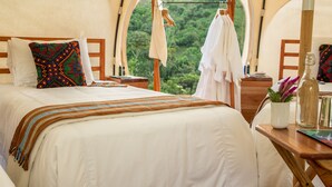 A tented accommodation room with a bed, a wooden nightstand, a hanging clothes rack, and a view of the forest. - Kinkara Luxury Retreat (El General)