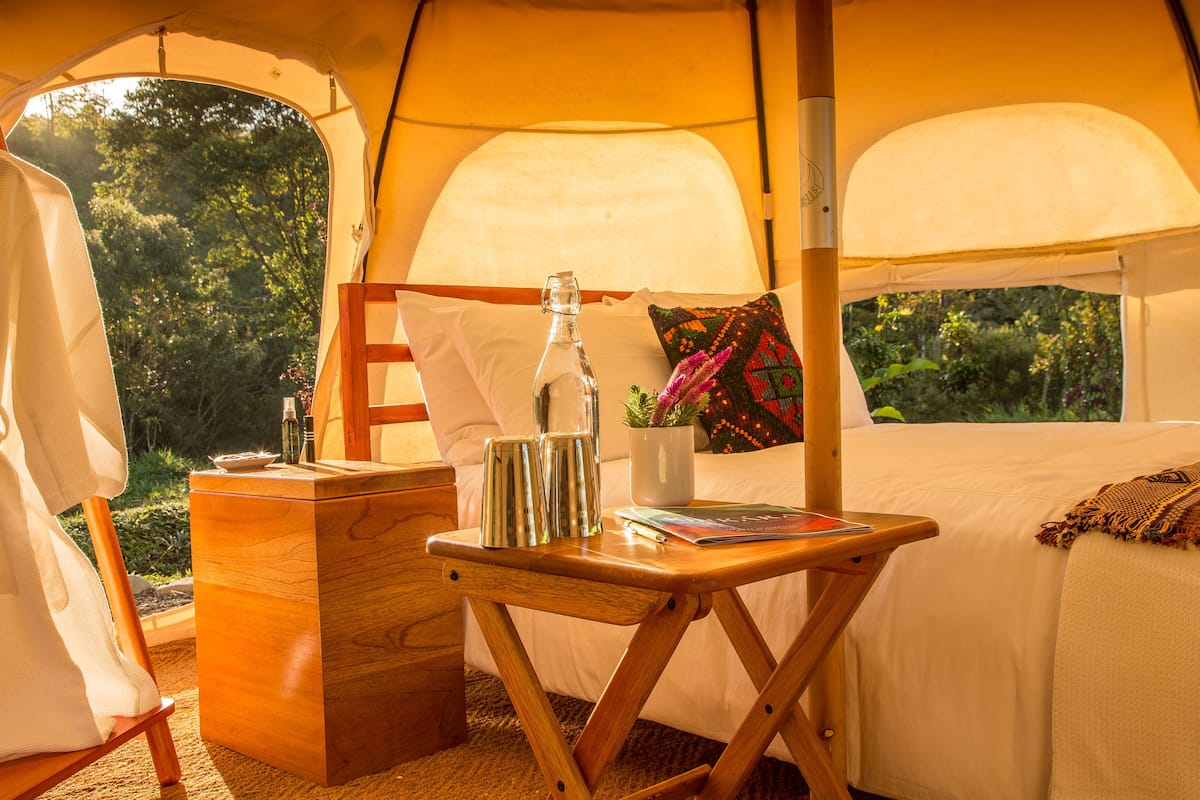 Eine Zelthütte mit Bett, einem kleinen Holztisch und einem Nachttisch.