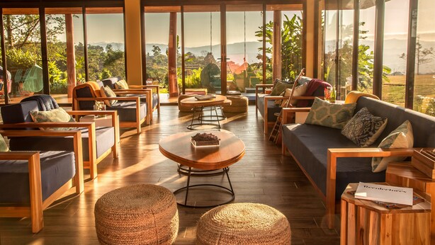 A spacious lounge area with wooden furniture, large windows offering a view of the outdoors, and a wooden floor. - Kinkara Luxury Retreat (El General)