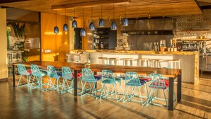 A modern kitchen with a wooden dining table and blue chairs, a large island with bar stools, and hanging pendant lights. - Kinkara Luxury Retreat (El General)