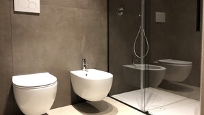 Un baño moderno con inodoro, bidé y zona de ducha con mampara de vidrio.