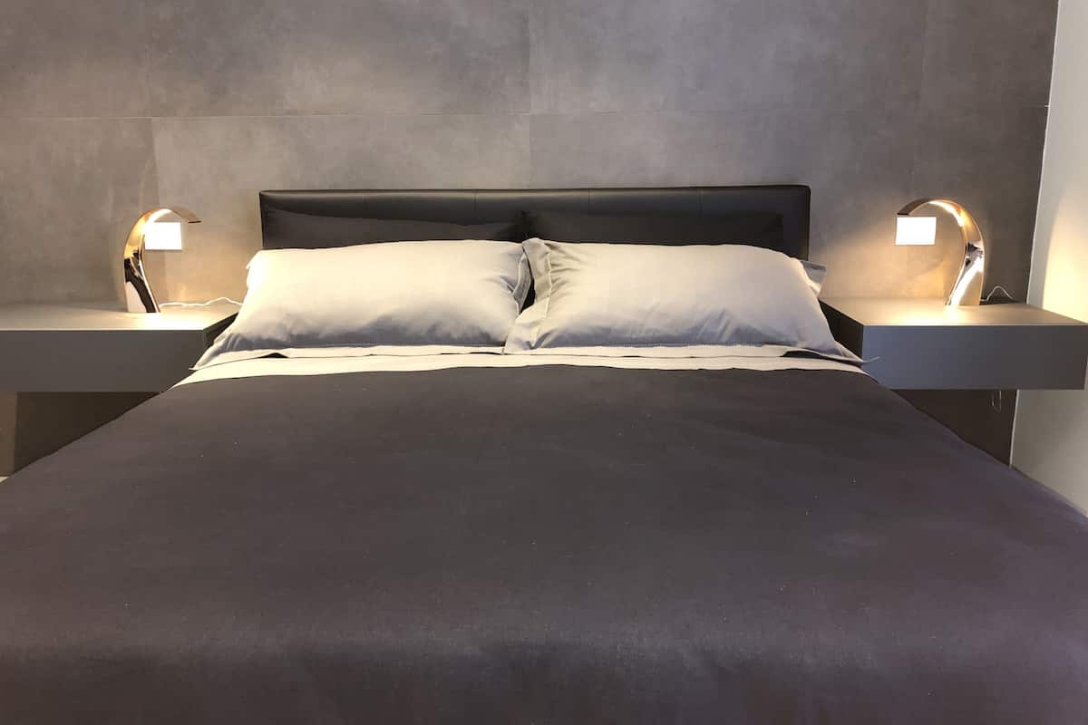 A modern bedroom with a large bed, two bedside tables, and wall-mounted lamps.