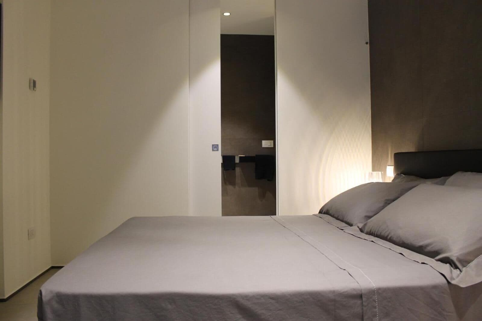 Una habitación de hotel con una cama, una mesita de noche y una lámpara en la pared.