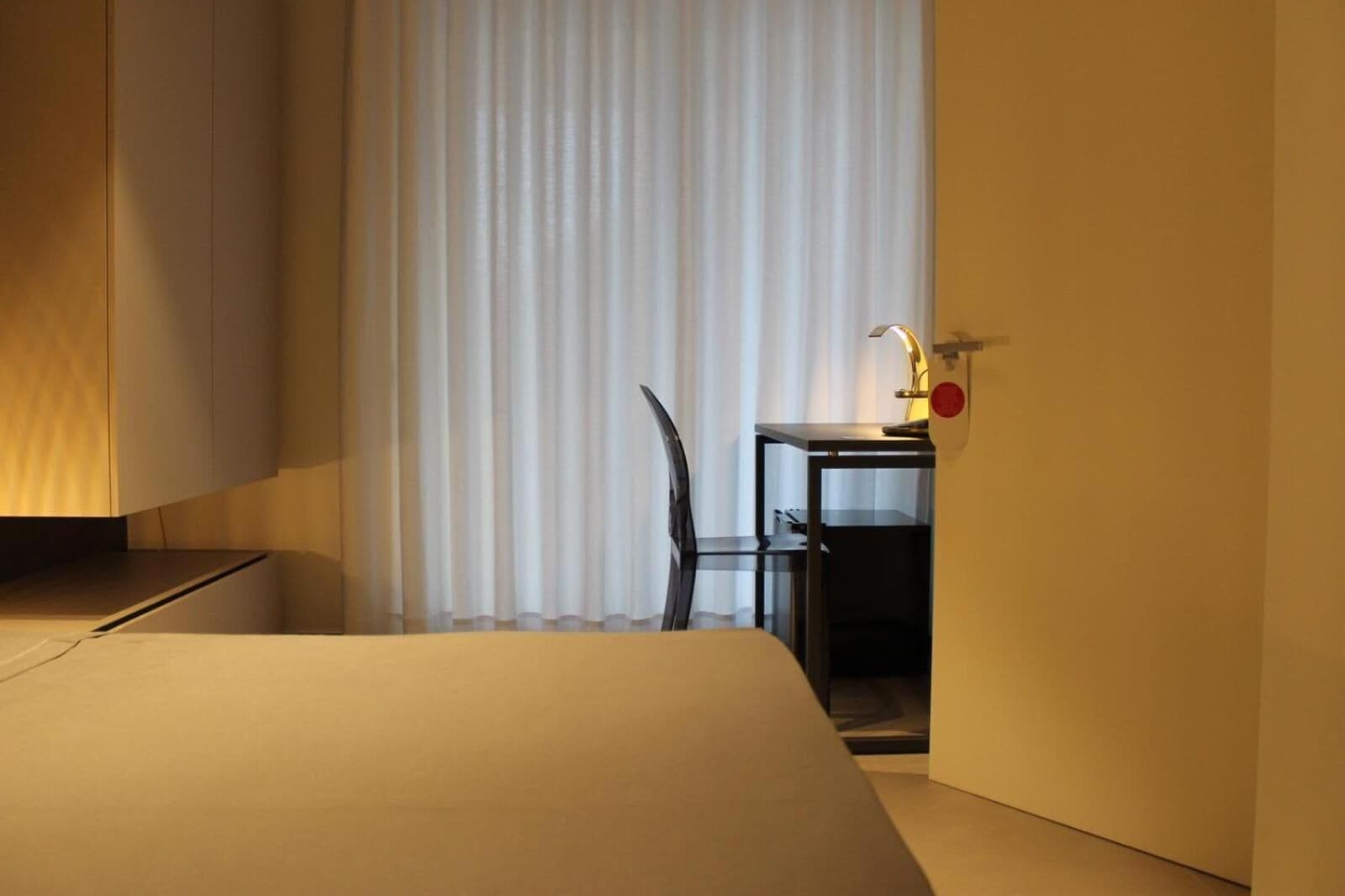 Une chambre d’hôtel avec un lit, un bureau et une chaise, ainsi qu’une fenêtre avec des rideaux.
