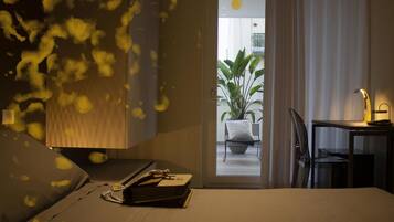 Habitación de hotel con cama, escritorio, silla y vista a un balcón con planta.