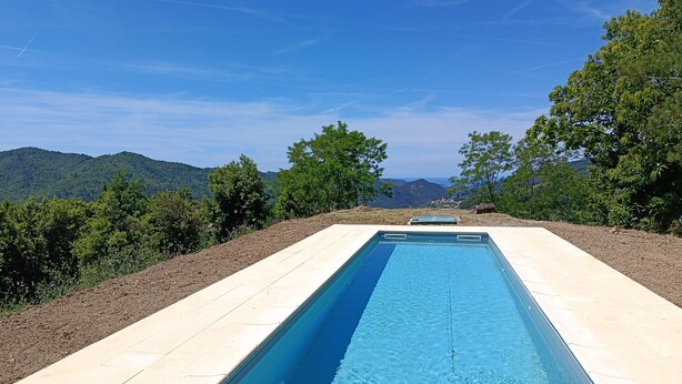 Una piscina rectangular con superficie de agua azul cristalina, rodeada por un patio cubierto de baldosas de color claro.