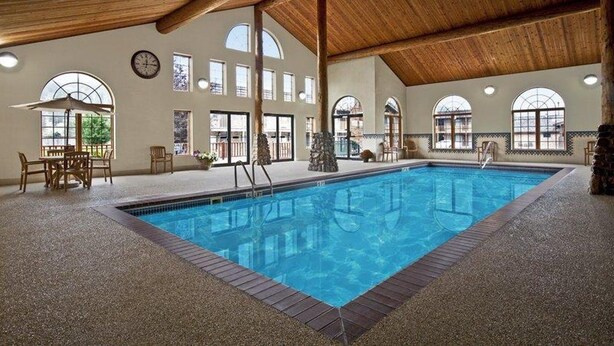 Una piscina interior con techo de madera, ventanas amplias y un área de estar con sillas y una mesa.