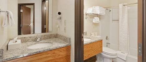 A modern bathroom with a granite countertop sink, a wooden vanity, a mirror, a toilet, and a shower area.