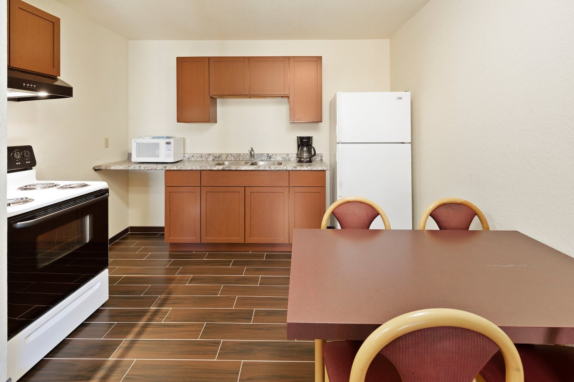 A compact kitchen with wooden cabinets, a white refrigerator, a microwave, and a stove. There is a dining table with two chairs.
