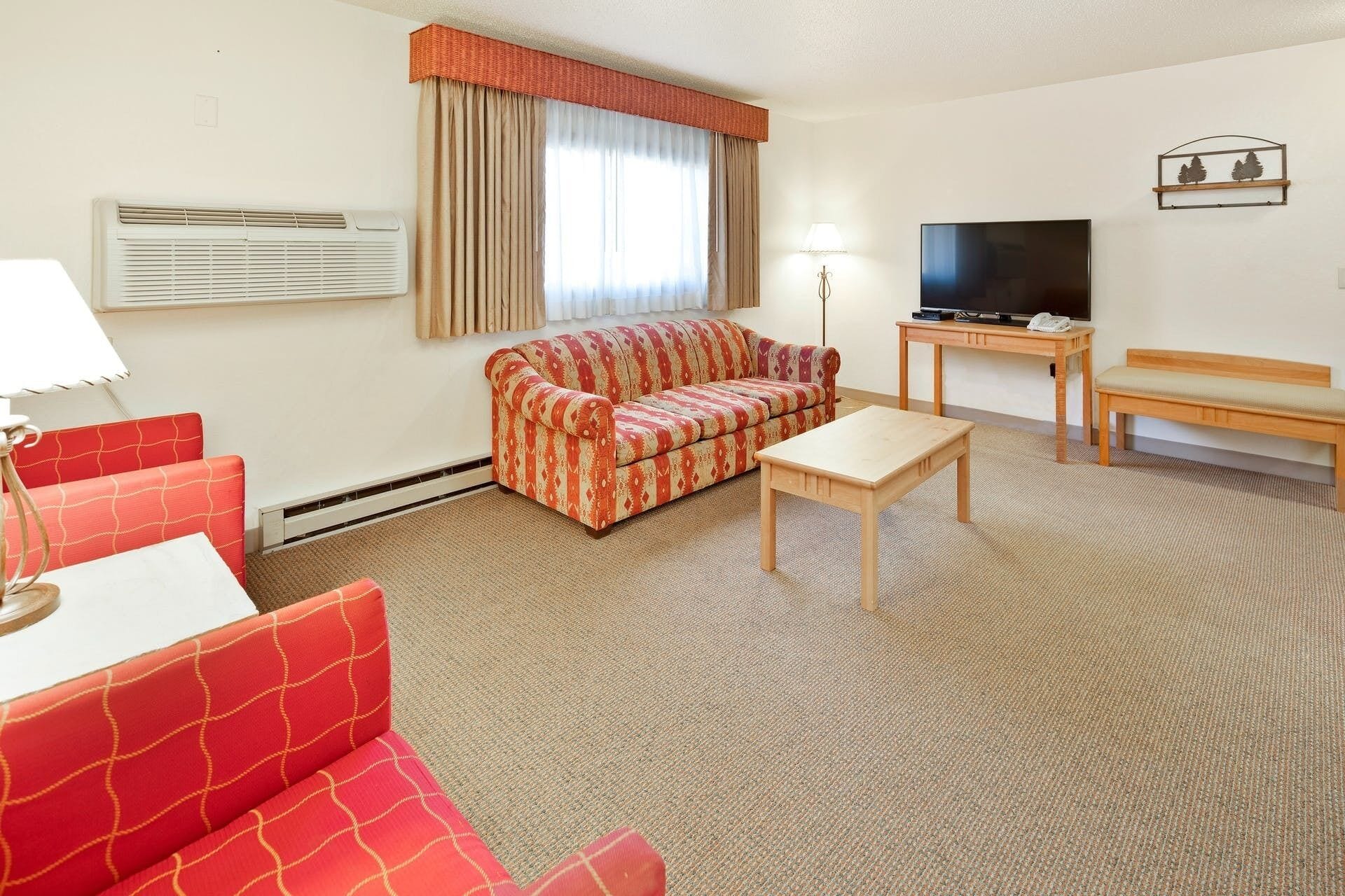 Ett hotellrum med en röd soffa med mönster, ett träbord, en tv och en lampa.