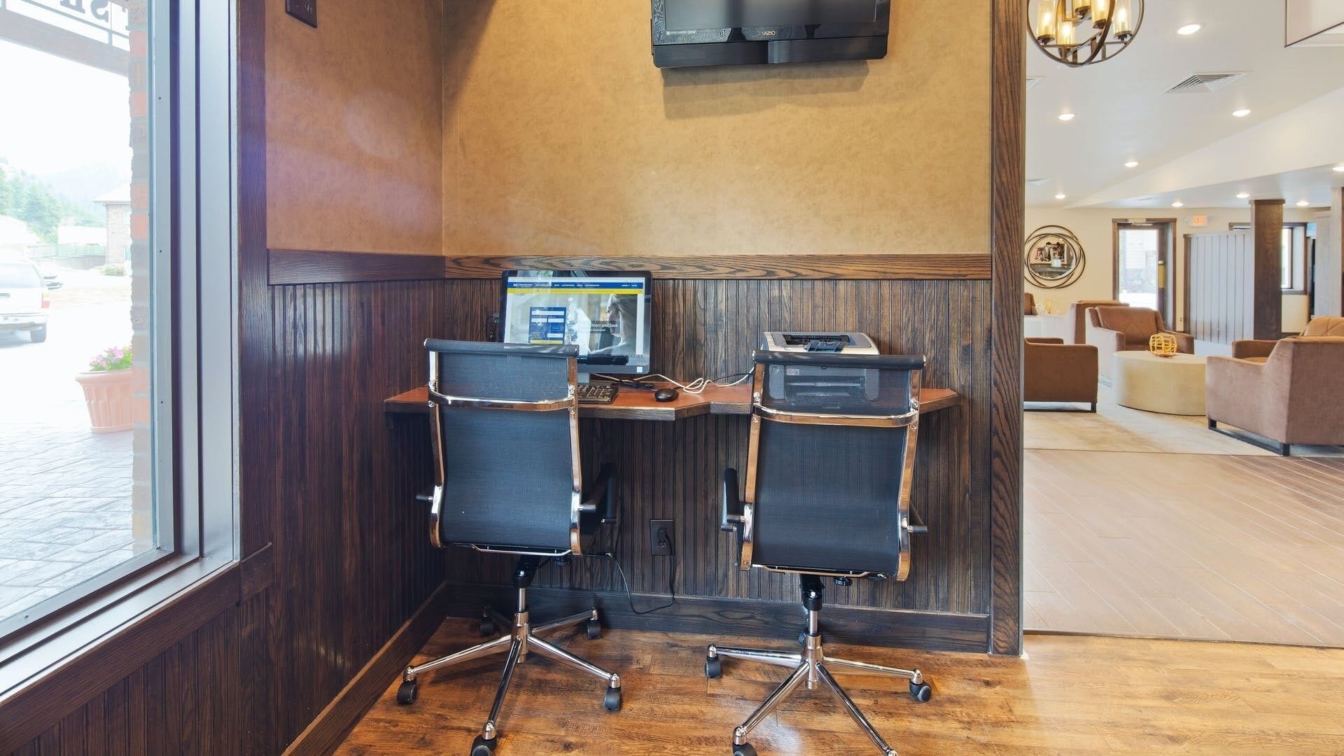 A modern office space with two black office chairs, a wooden desk, and a mounted flat-screen TV.