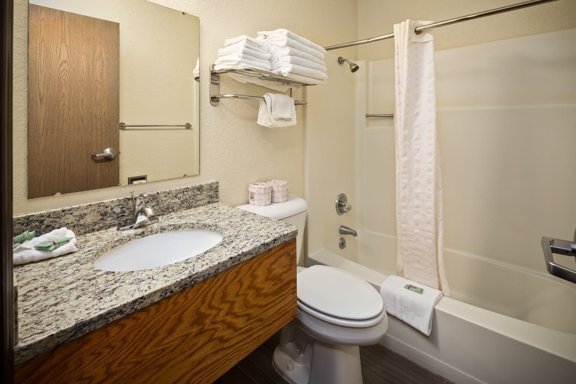 A bathroom with a granite countertop, two sinks, a toilet, a shower with a glass door, and a towel rack with folded towels.