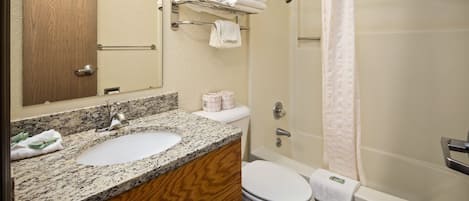 A bathroom with a granite countertop, two sinks, a toilet, a shower with a glass door, and a towel rack with folded towels.
