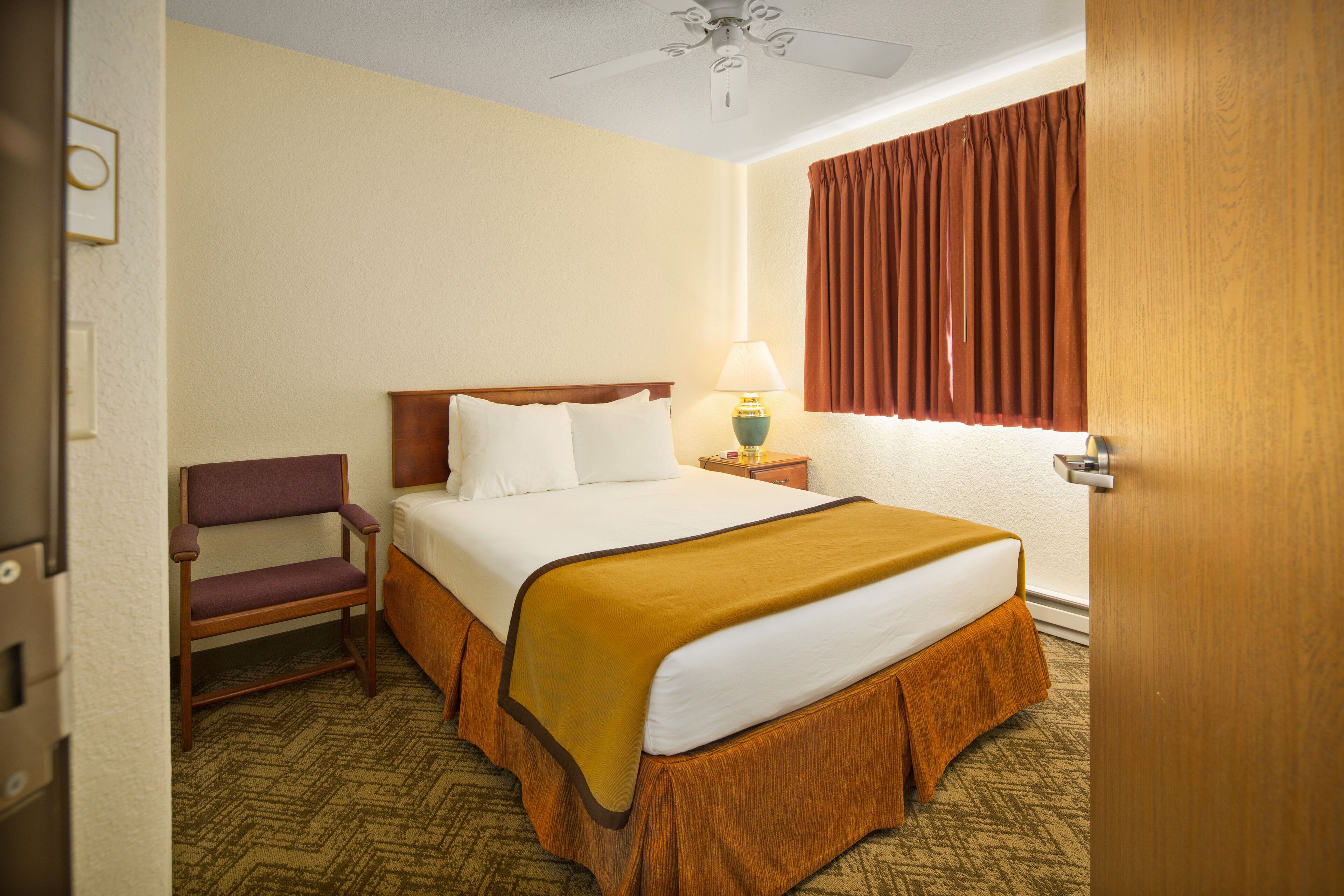 A hotel room with a bed, a nightstand, a lamp, a chair, and a window with curtains.