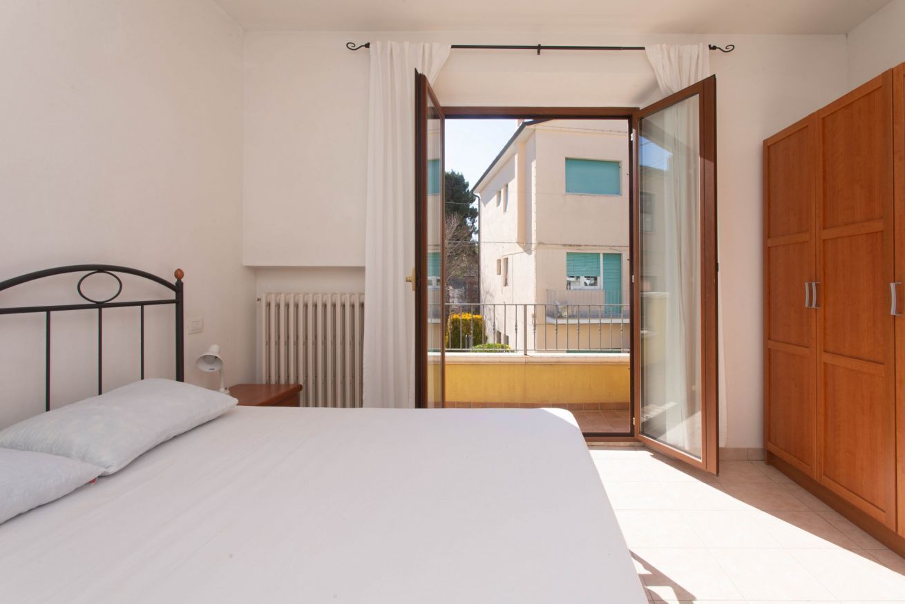 Una camera da letto con un letto, un armadio in legno, un termosifone e una porta scorrevole in vetro che dà su un balcone esterno.