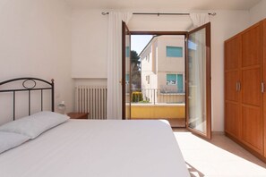 A bedroom with a bed, a wooden wardrobe, a radiator, and a sliding glass door leading to an outdoor balcony.