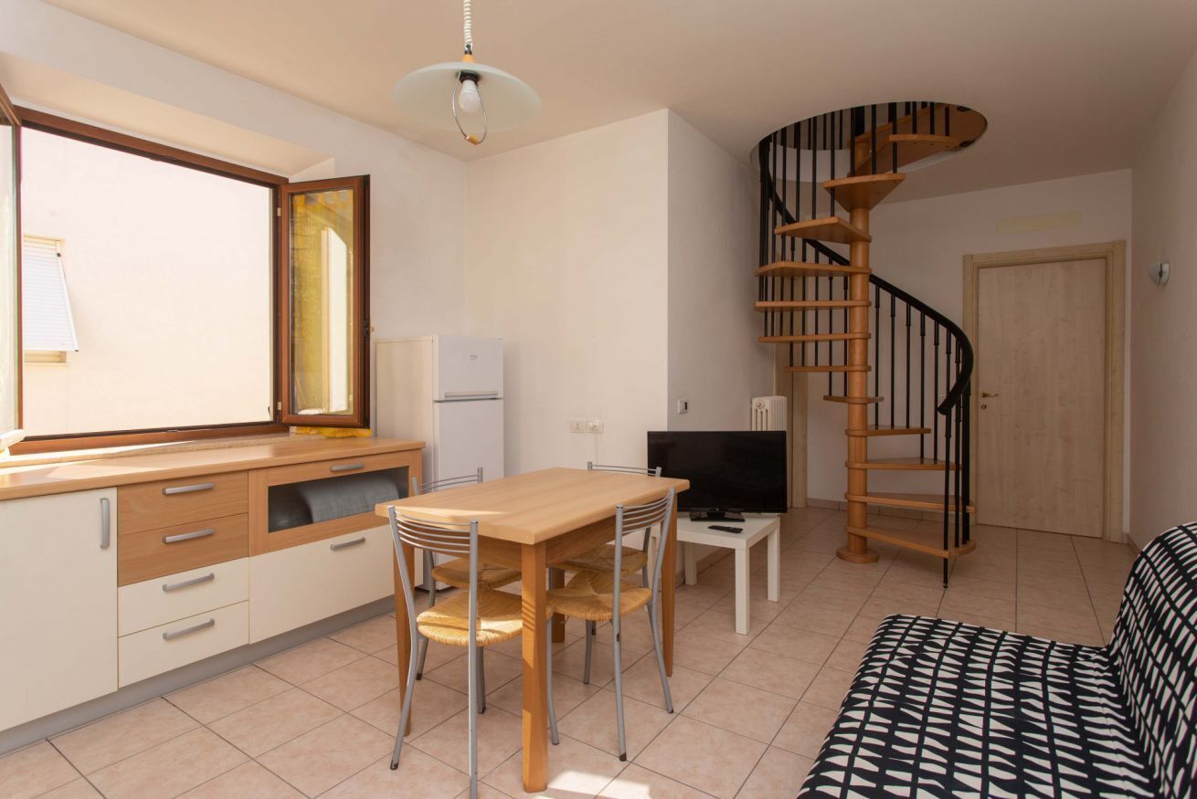 Ett kompakt bostadsutrymme med kök, matplats och en spiraltrappa.