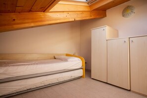 A room with a bed, wooden ceiling beams, a wardrobe, and a skylight.