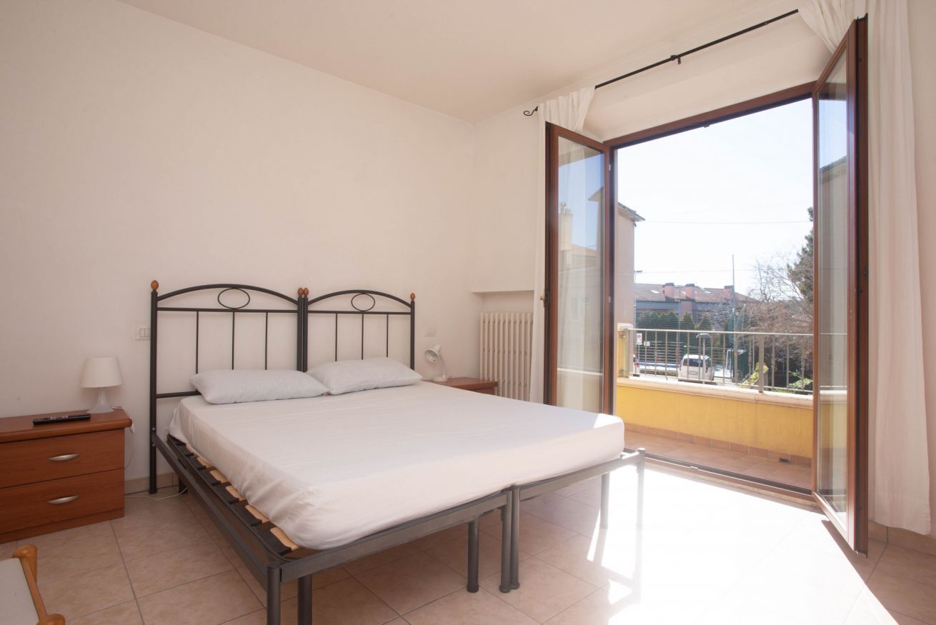 Una camera da letto con un letto, un comodino, una lampada e vista su un balcone.