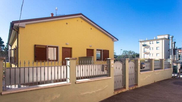 A yellow building with a gated entrance, a small balcony, and a neighboring taller building. - N032 - Numana, new three-room apartment with terrace on the left (Numana)
