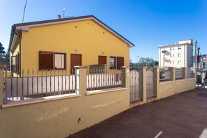 A yellow building with a gated entrance, a small balcony, and a neighboring taller building.