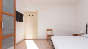A bedroom with a bed, a chair, a wooden door, a TV mounted on the wall, and a small bedside table with a lamp. - N032 - Numana, new three-room apartment with terrace on the left (Numana)