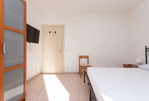 A bedroom with a bed, a chair, a wooden door, a TV mounted on the wall, and a small bedside table with a lamp. - N032 - Numana, new three-room apartment with terrace on the left (Numana)
