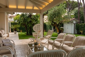 Eine Terrasse im Freien mit Korbmöbeln, einem Glastisch und einem weißen Pavillon.