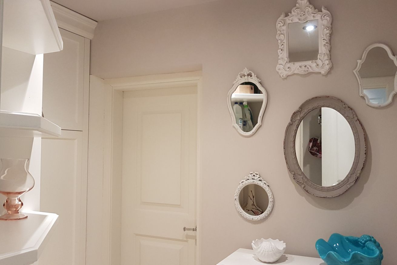 A bathroom with a white door, a sink with a blue vase, and three mirrors on the wall.