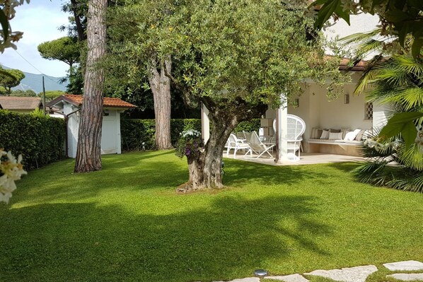 A well-maintained garden with a lawn, a white outdoor seating area, and a building with a tiled roof.