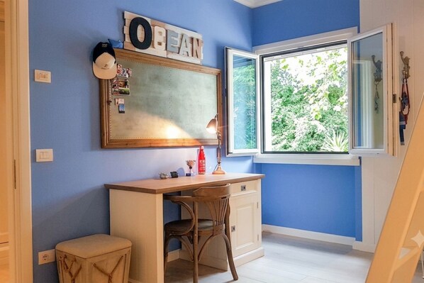 Una habitación con escritorio, silla, ventana y un espejo en la pared.