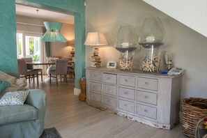 A living room with a sofa, a dining area with chairs, a staircase, and a cabinet with decorative items.