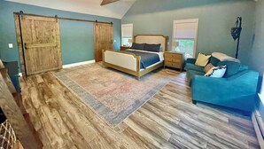 A bedroom with a bed, a blue sofa, a wooden ceiling beam, and a ceiling fan. - Southold, NY- Heart of North Fork Wine Country and Minutes From The Beach (Southold)
