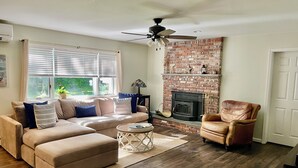 A living room with a brick fireplace, a ceiling fan, a sofa, a leather armchair, and a coffee table. - Southold, NY- Heart of North Fork Wine Country and Minutes From The Beach (Southold)