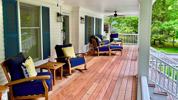 A covered porch with wooden furniture, ceiling fans, and a view of greenery. - Southold, NY- Heart of North Fork Wine Country and Minutes From The Beach (Southold)