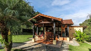 A covered outdoor patio with a dining area, surrounded by greenery and a stone pathway. - Beautiful Chalet in El Caimo (El Caimo)