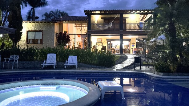A pool area with lounge chairs and a hot tub, surrounded by lush greenery and a two-story building with outdoor seating. - Beautiful Chalet in El Caimo (El Caimo)