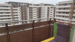 Un balcón con cerramiento de madera, un banco amarillo y verde, y vistas a edificios de varios pisos.