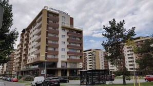 Un edificio residencial urbano de varios pisos con balcones, una zona de estacionamiento y un pequeño quiosco.