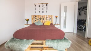 Una cama con una colcha roja, cabecera de madera y almohadas mullidas. Encima de la cama, un collage de fotos colgado en la pared.