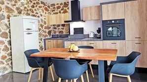 Eine moderne Küche mit Steinrückwand, Holzschränken, einem eingebauten Ofen und einem Essbereich mit Holztisch und blauen Stühlen.