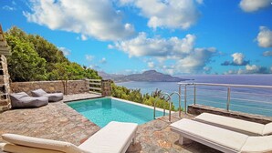 Ein Poolbereich mit Liegestühlen und einer Steinmauer mit Blick auf das Meer.