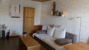 Una sala de estar acogedora con un sofá de madera, una mesa de madera y una estantería decorativa con figuritas.