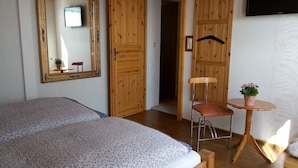 Un dormitorio con una cama, una silla, una mesita con una planta y un televisor en la pared.